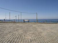 a bench on a cobblestone road next to the ocean with a view of mountains