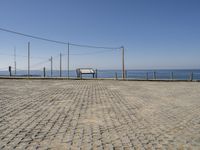 a bench on a cobblestone road next to the ocean with a view of mountains