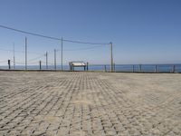 a bench on a cobblestone road next to the ocean with a view of mountains