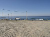 a bench on a cobblestone road next to the ocean with a view of mountains