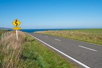 road sign on a country roadway with sea behind it and grassy field in the foreground