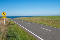 road sign on a country roadway with sea behind it and grassy field in the foreground