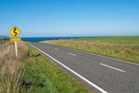 road sign on a country roadway with sea behind it and grassy field in the foreground