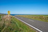 road sign on a country roadway with sea behind it and grassy field in the foreground