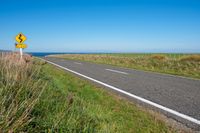 road sign on a country roadway with sea behind it and grassy field in the foreground