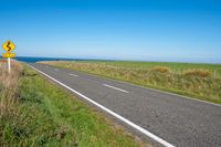 road sign on a country roadway with sea behind it and grassy field in the foreground