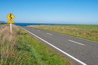 road sign on a country roadway with sea behind it and grassy field in the foreground