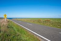 road sign on a country roadway with sea behind it and grassy field in the foreground