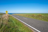 road sign on a country roadway with sea behind it and grassy field in the foreground