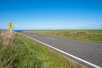 road sign on a country roadway with sea behind it and grassy field in the foreground