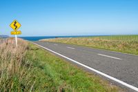 road sign on a country roadway with sea behind it and grassy field in the foreground