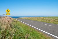 road sign on a country roadway with sea behind it and grassy field in the foreground