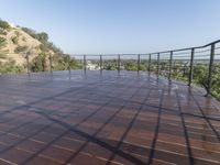 a deck with water pouring in and railing along the bottom of it and below a hillside