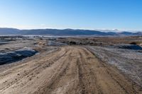 a dirt road winding around the side of a mountain and snow covered terrain in the background