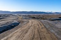 a dirt road winding around the side of a mountain and snow covered terrain in the background