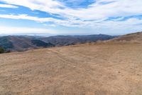 a brown dirt path through some grassy hills and mountains and a blue sky with clouds