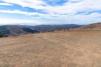 a brown dirt path through some grassy hills and mountains and a blue sky with clouds