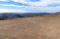 a brown dirt path through some grassy hills and mountains and a blue sky with clouds