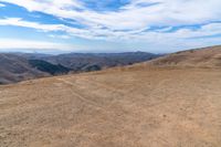 a brown dirt path through some grassy hills and mountains and a blue sky with clouds