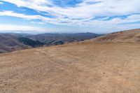 a brown dirt path through some grassy hills and mountains and a blue sky with clouds