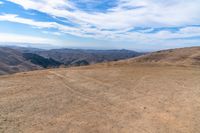 a brown dirt path through some grassy hills and mountains and a blue sky with clouds