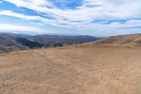 a brown dirt path through some grassy hills and mountains and a blue sky with clouds