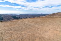 a brown dirt path through some grassy hills and mountains and a blue sky with clouds