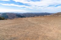 a brown dirt path through some grassy hills and mountains and a blue sky with clouds