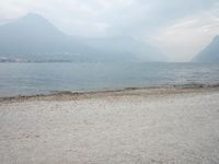 an empty bench on the beach of a lake in the background is mountains and a city in the distance