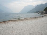 an empty bench on the beach of a lake in the background is mountains and a city in the distance