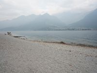 an empty bench on the beach of a lake in the background is mountains and a city in the distance