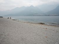 an empty bench on the beach of a lake in the background is mountains and a city in the distance