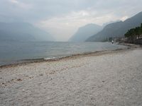 an empty bench on the beach of a lake in the background is mountains and a city in the distance