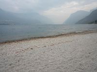 an empty bench on the beach of a lake in the background is mountains and a city in the distance