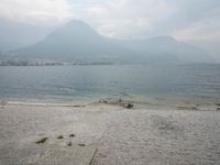 an empty bench on the beach of a lake in the background is mountains and a city in the distance