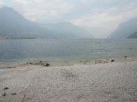 an empty bench on the beach of a lake in the background is mountains and a city in the distance