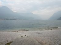 an empty bench on the beach of a lake in the background is mountains and a city in the distance