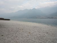 an empty bench on the beach of a lake in the background is mountains and a city in the distance