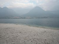 an empty bench on the beach of a lake in the background is mountains and a city in the distance