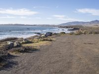 a paved dirt road with a bench and some mountains and waves in the water behind it