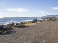 a paved dirt road with a bench and some mountains and waves in the water behind it