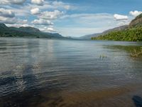 a body of water that is near some mountains and a river with trees on the shore