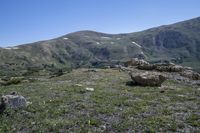 mountains are covered with green grass and rocks with snow on the slopes in the distance