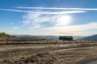 dirt road leading to a pasture with mountains in the distance near an empty field of grass