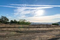 dirt road leading to a pasture with mountains in the distance near an empty field of grass