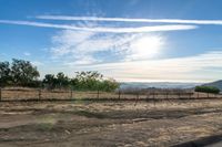 dirt road leading to a pasture with mountains in the distance near an empty field of grass