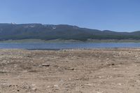 mountains and lake in a desert field with brown dirt and grass in front of water