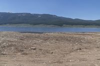 mountains and lake in a desert field with brown dirt and grass in front of water