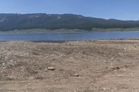 mountains and lake in a desert field with brown dirt and grass in front of water