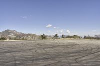 a view along a dirt road of an empty field and mountains in the distance of the scene